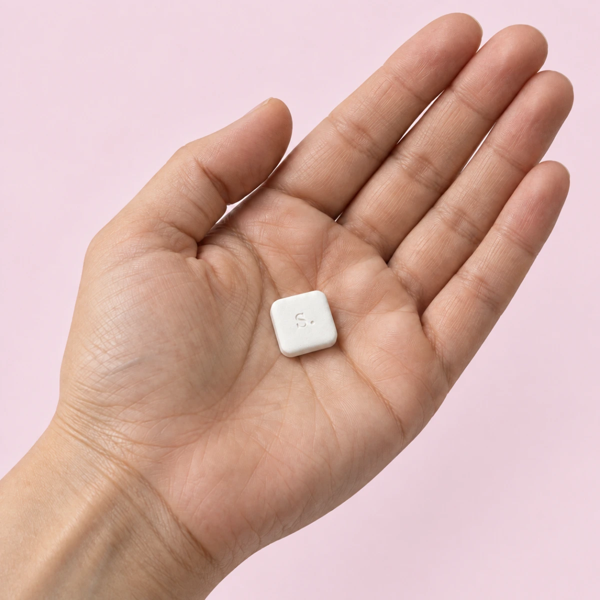 A generated adult open hand holding one small white tablet against a soft pink background.