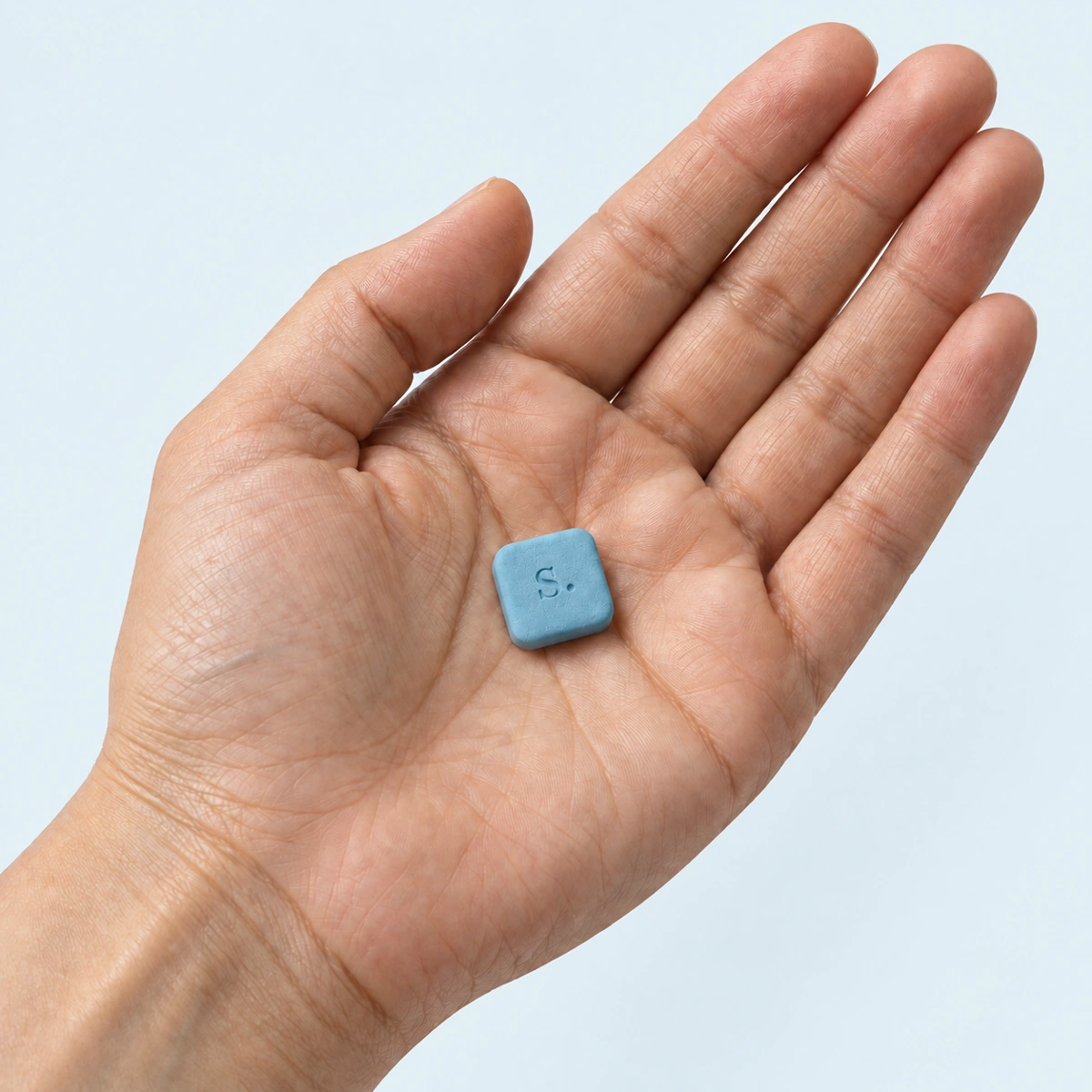 Illustrative adult hand holding one small blue signal-rx tablet against pale blue.