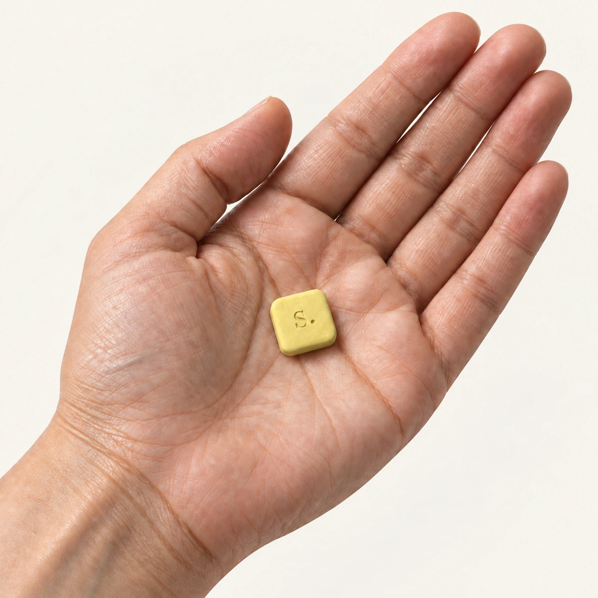 Illustrative adult hand holding one small yellow signal-rx tablet against cream.